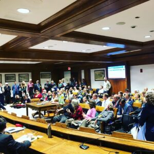 A room full of people seated for testimony at the Massachusetts state house.